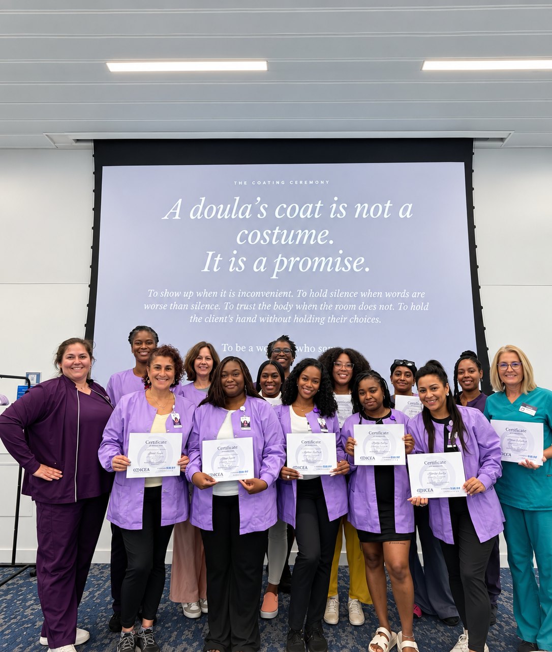 Madeline Harris LeBlanc with a graduating cohort of Mary&rsquo;s Hands Network community doulas in lavender scrub jackets, holding their ICEA certificates at the coating ceremony